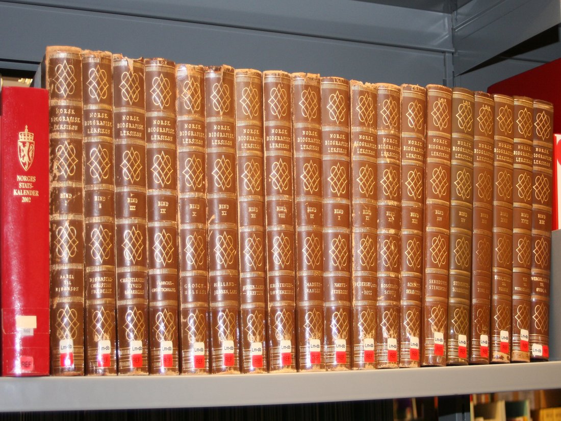 Uma fileira de volumes encadernados de uma enciclopédia impressa numa estante de biblioteca
